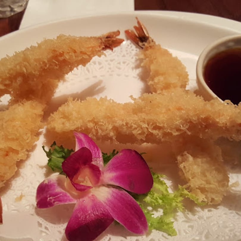 Crispy tempura shrimp with a side of dipping sauce, garnished with lettuce and an orchid.
