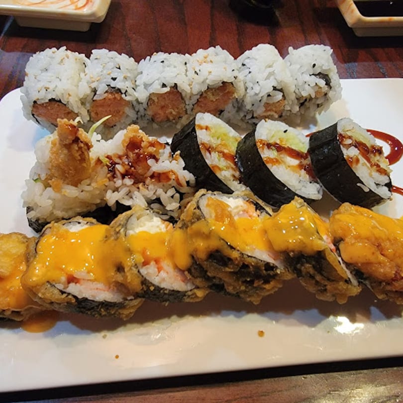 A white plate holds three rows of sushi rolls, including fried and sauced varieties.